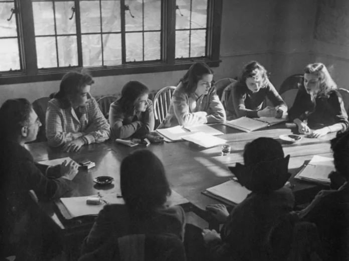 students gathered around a conference table smoking, 1950s