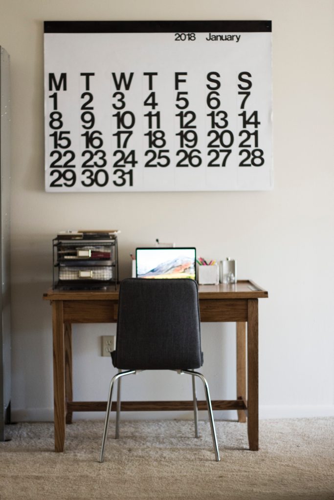 Chair and desk with calendar on the wall.