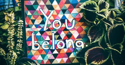 colorful sign saying "you belong" surrounded by plants