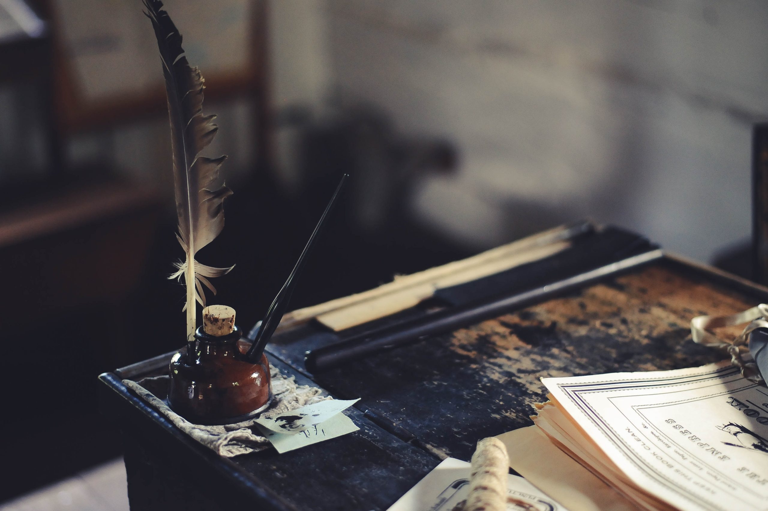 old desk with feather pen in an inkwell beside a tattered notebook.