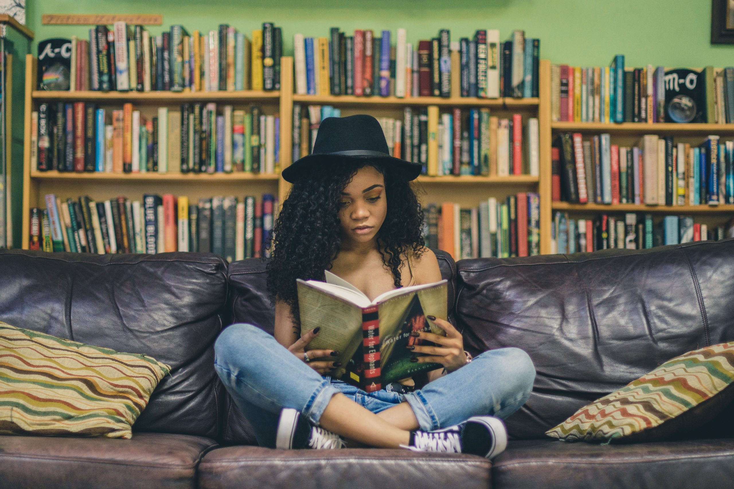 Woman reading while sitting on a couch, with bookshelves filling the background.