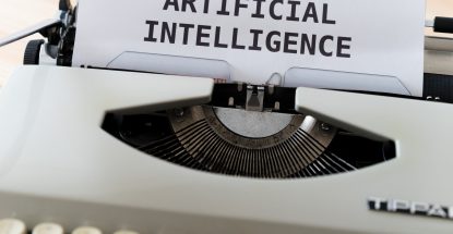 A manual typewriter with the words "artificial intelligence" typed in large-sized font on an otherwise blank white page.