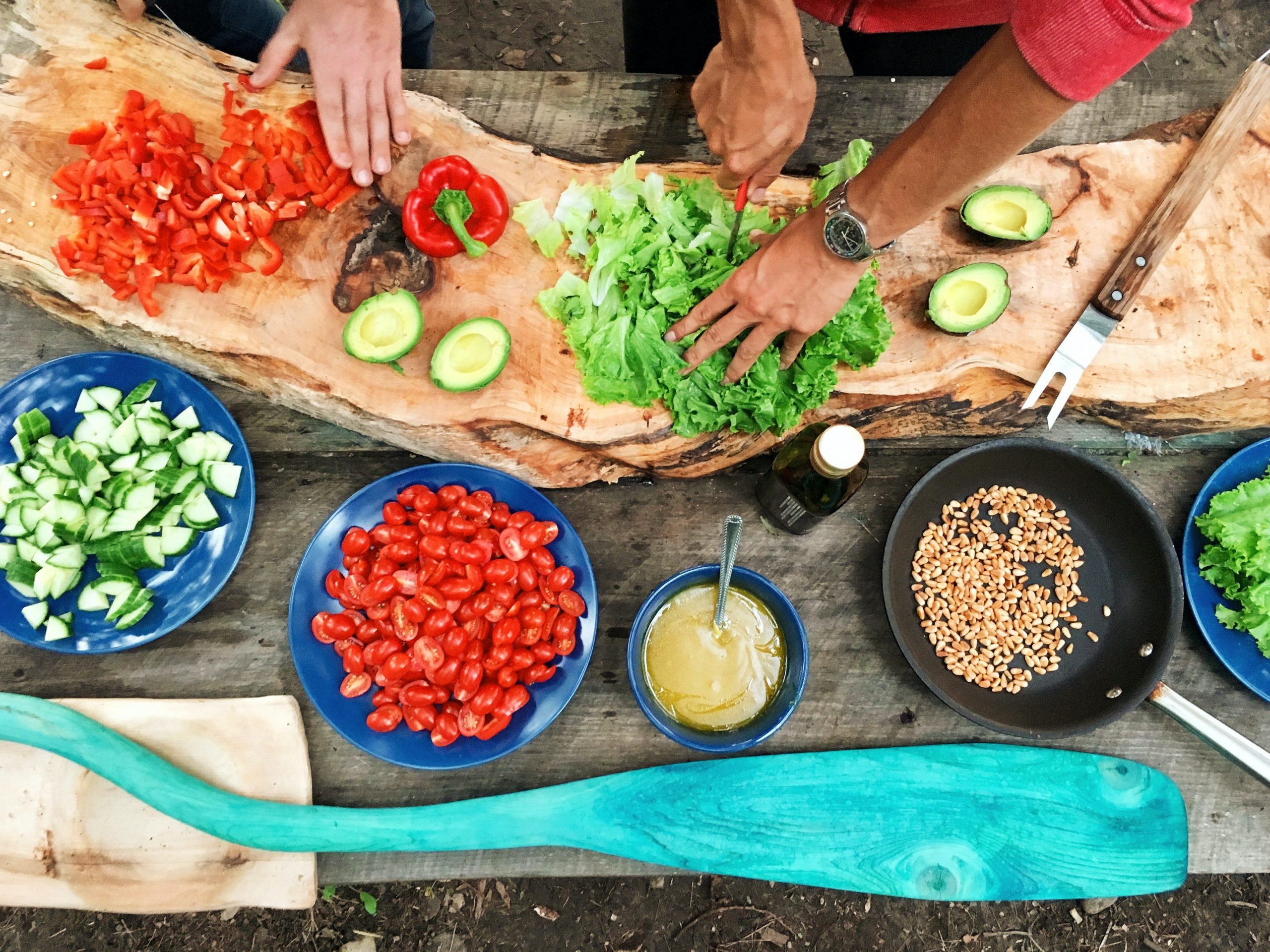 Two pairs of hands preparing food on a table filled with fresh ingredients.